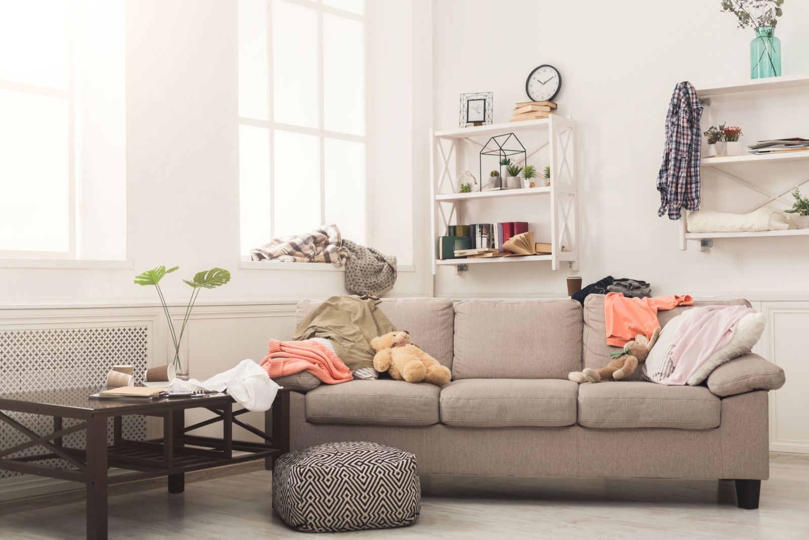 living room with a gray couch, a lot of toys all over the room, cluttered, white shelves on the wall