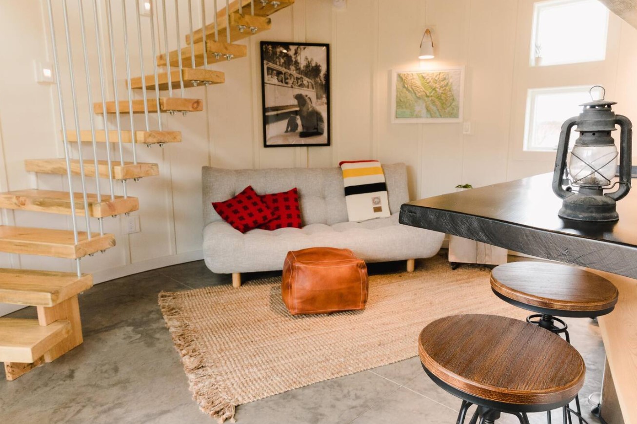 open concept living room with a gray couch, a brown, leather sitting area in front, and stairs leading up to the loft