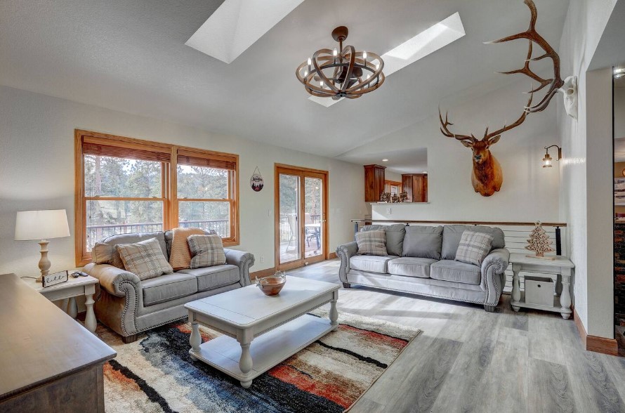 living room with gray couches, light gray table in the middle of the room and mini gray tables next to the couches, deer and deer antlers on the white walls of the room