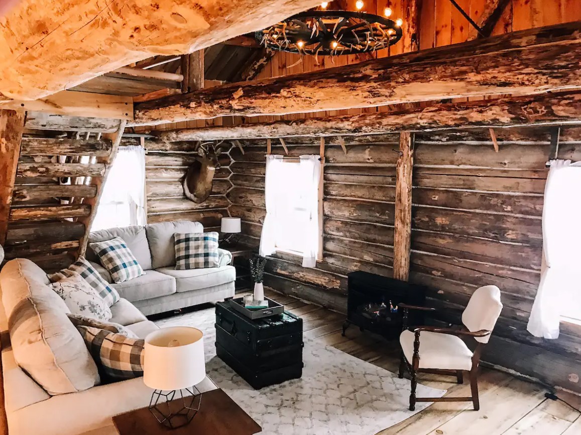 living room with an off-white couch, a chair next to the black fireplace, mini brown table and wooden walls