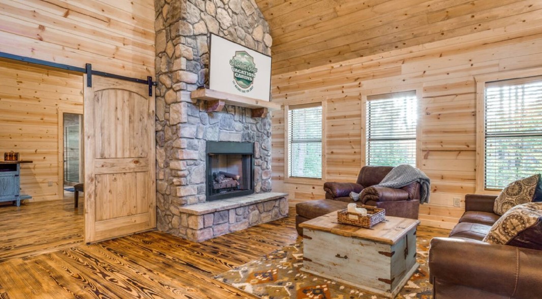 living room with wooden walls, wooden ceiling, fireplace, wooden table and brown leather couches