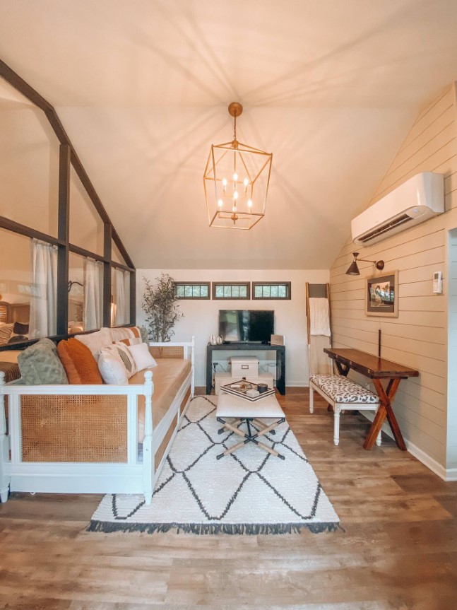 living room with a beige and white couch, small white table in the middle of the room and a mini brown table on the right, beautiful chandelier on top and an ac on the right wall