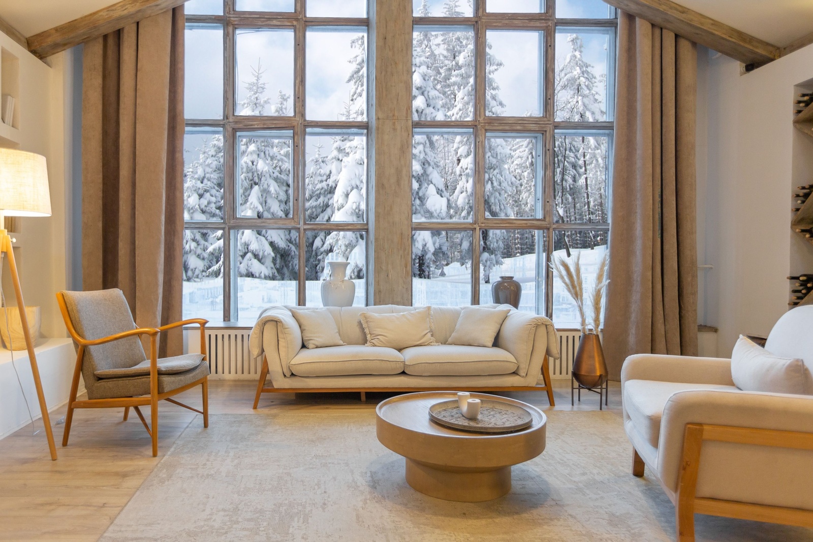 living room with a floor to ceiling with snow view, beige and gray furniture, wooden round table