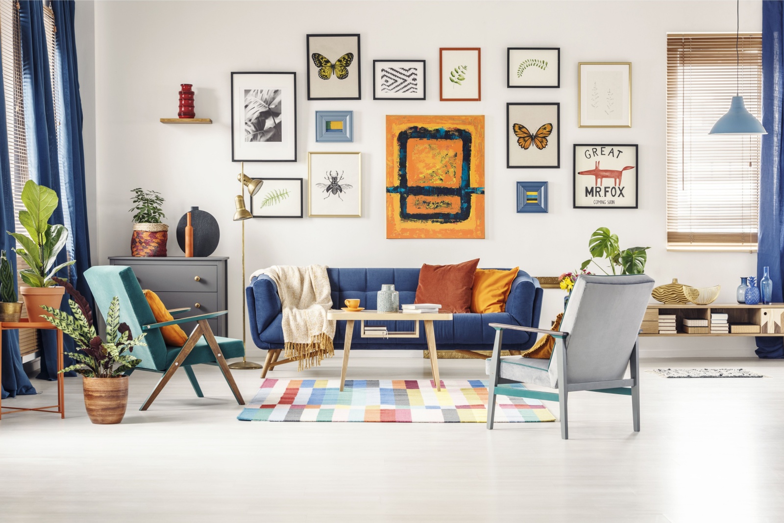 living room with a gallery wall, blue couch, gray cabinet, two chairs, colorful and maximalist interior