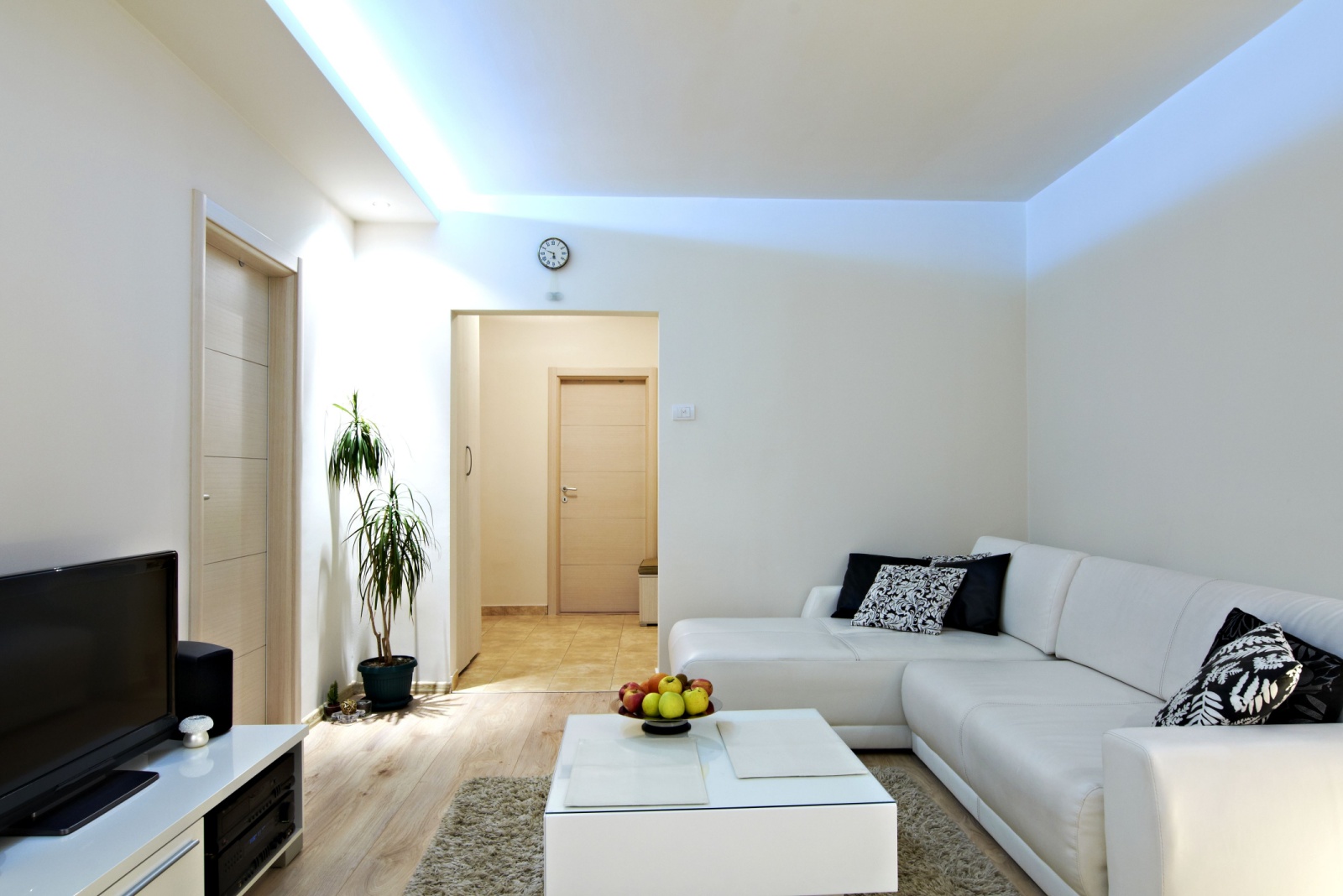 living room with a white l-shaped couch, white table, white cabinet with a tv, led lights