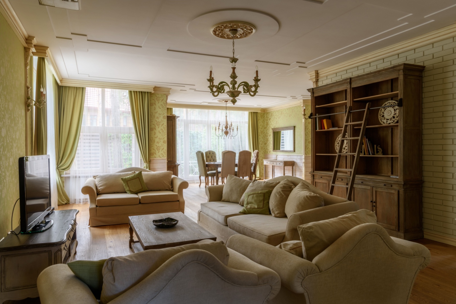 living room with green floral walls, green curtains, light green couch and sofas, brown cabinet with open shelves, luxurious chandelier