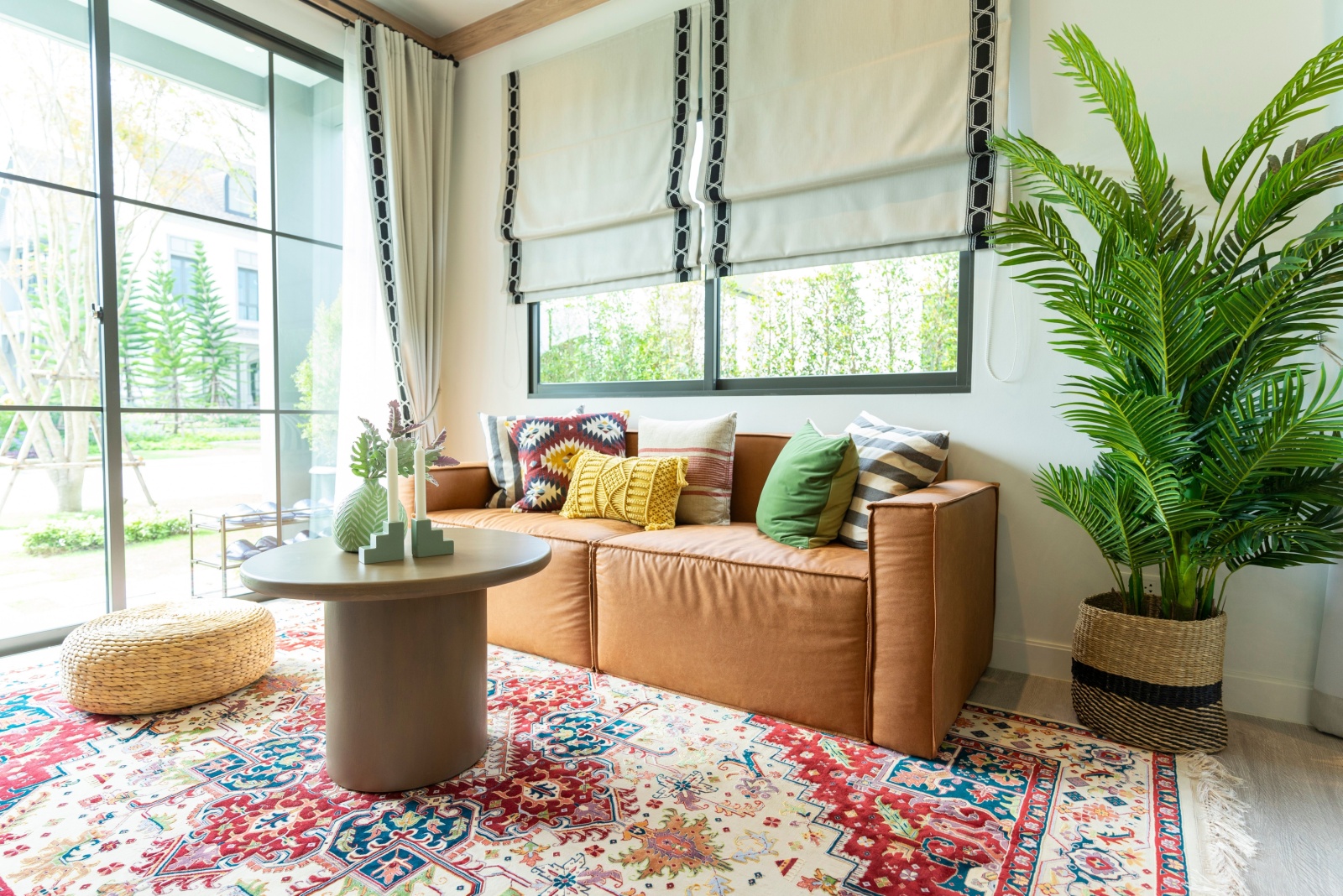 living room with a textured carpet, brown couch, round brown table, big plant, colorful pillows