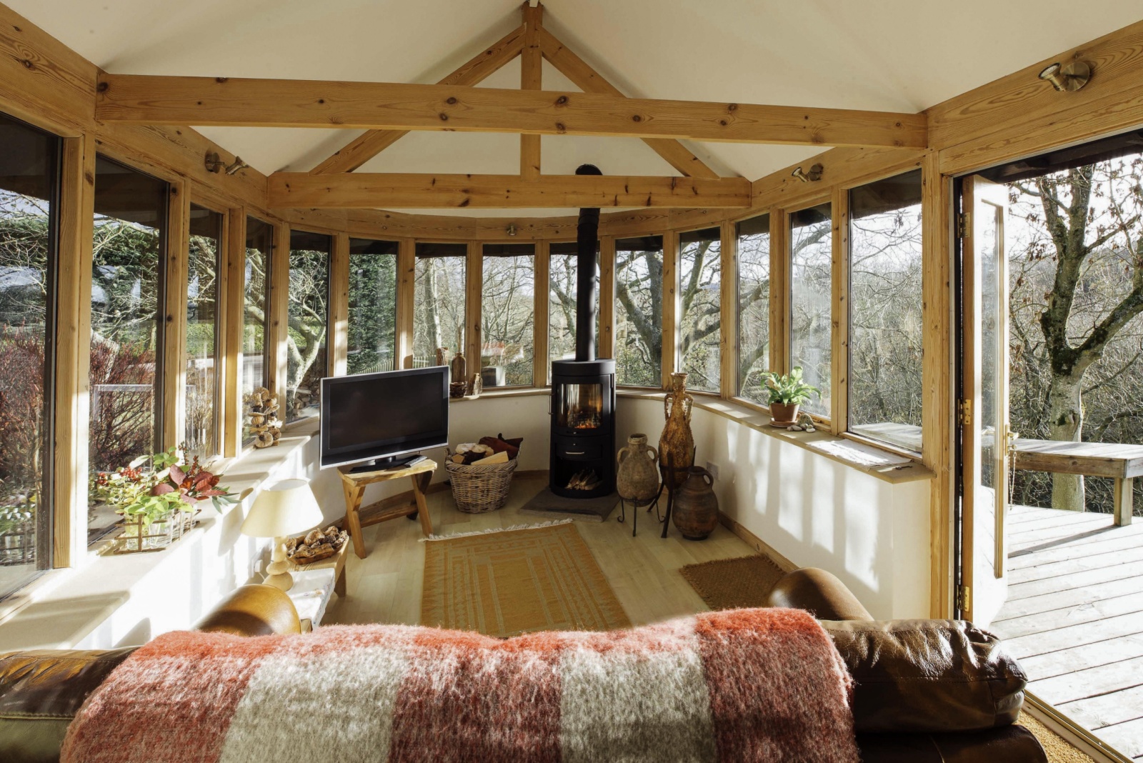 living room with windows all around, flat-screen tv, black fireplace, wood beams, brown carpet