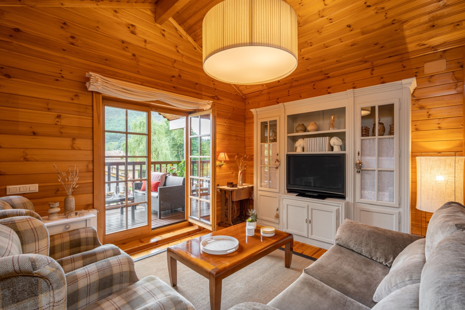 living room with brown, wooden walls, gray couch and sofas, brown table and white cabinet