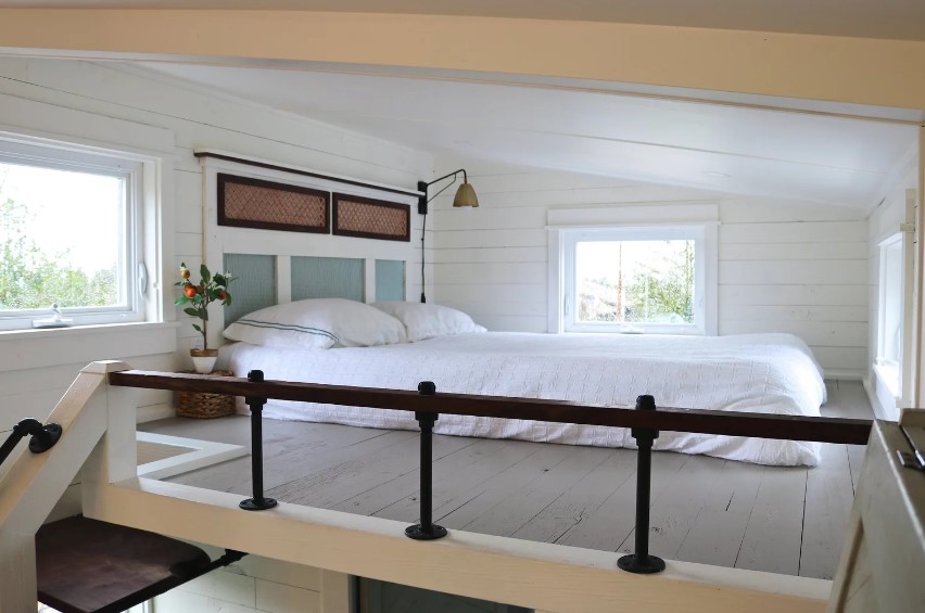 loft bedroom with white wooden walls, white bed sheets and windows