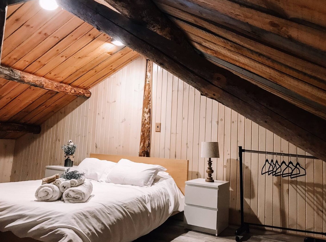 loft bedroom with a slanted roof and a big bed, white bedside table