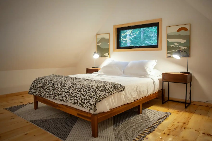 loft bedroom with a queen-sized bed, two bedside tables, window above the bed and two art pieces around the window