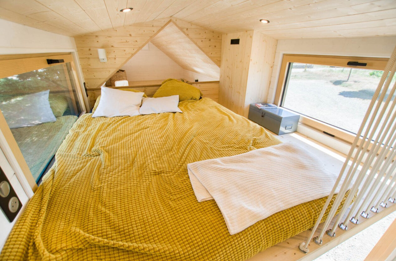 loft bedroom with windows on both sides and a big bed with a yellow bedsheet