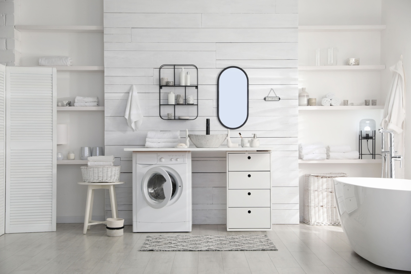 all white bathroom with a white bathtub, white drawers and a white countertop, white built-in shelves, a washing machine, a mirror above the countertop