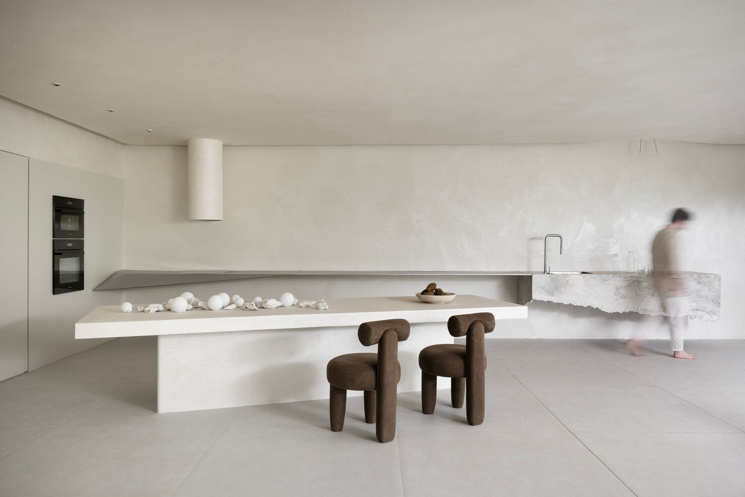 minimalist kitchen with a unique off-white table and walls, two brown chairs