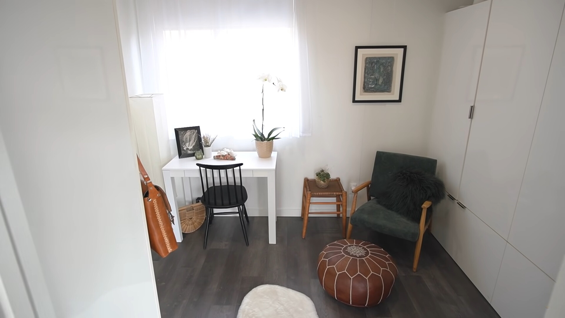 office room with a white desk accompanied by a black chair, black sofa in the corner with a small brown stool, floor to ceiling white closet