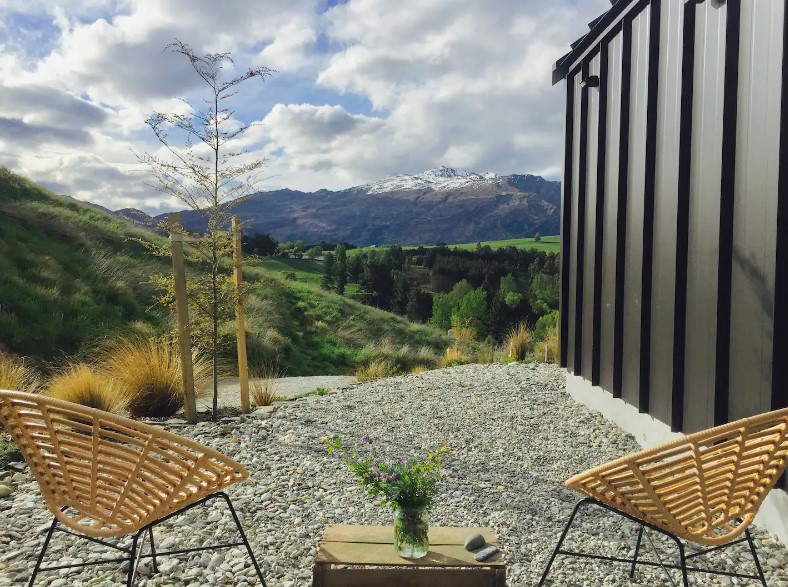 outdoors area of a tiny home with two brown chairs and a mini table overlooking the beautiful nature