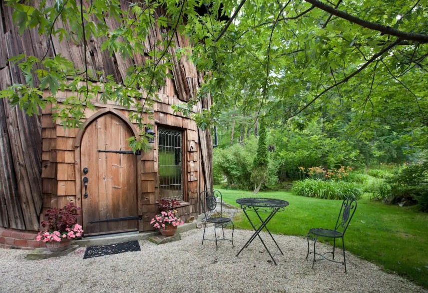 outside area of a round cabin with a table and two chairs, surrounded by greenery