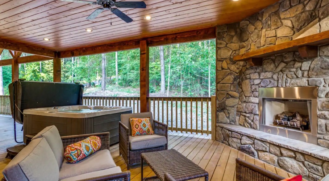 outside deck area of a log cabin with sitting spaces, a fireplace and a hot tub