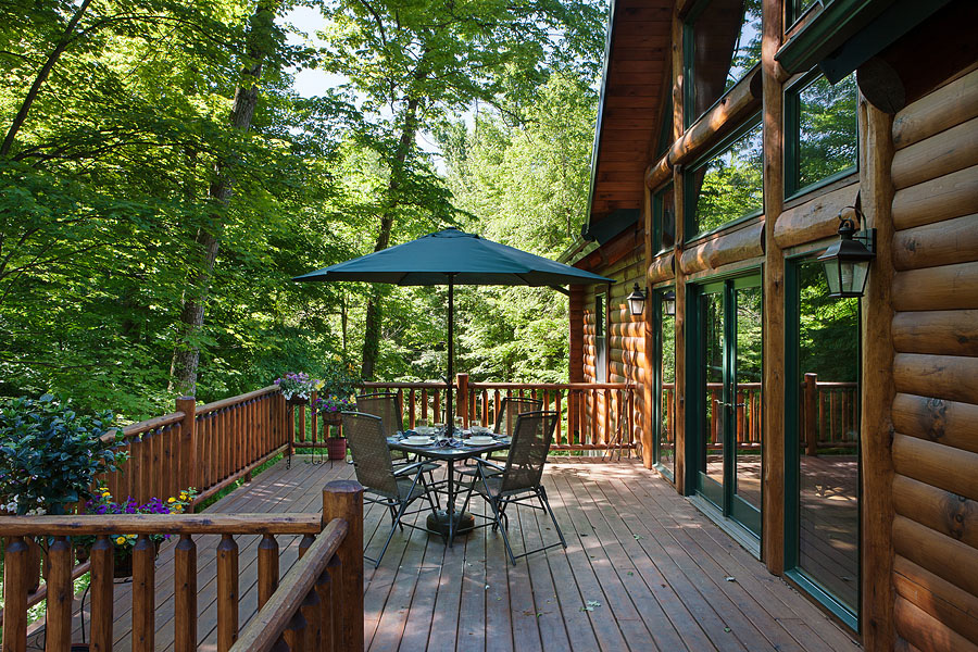 porch with a table, parasol and chairs around a table and greenery in front of the house