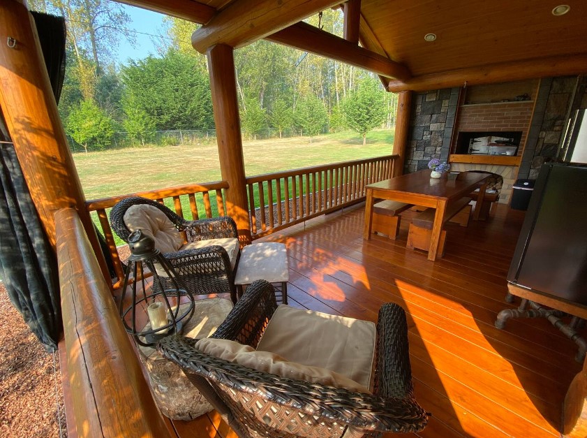 porch of a cabin with a long dining table, benches with the table, two chairs in the corner and a tiny table