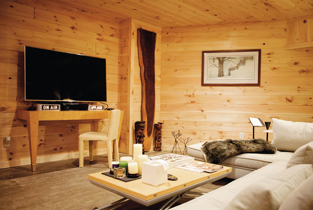 room with a flat screen tv, wooden walls, wooden table and an l-shaped beige couch