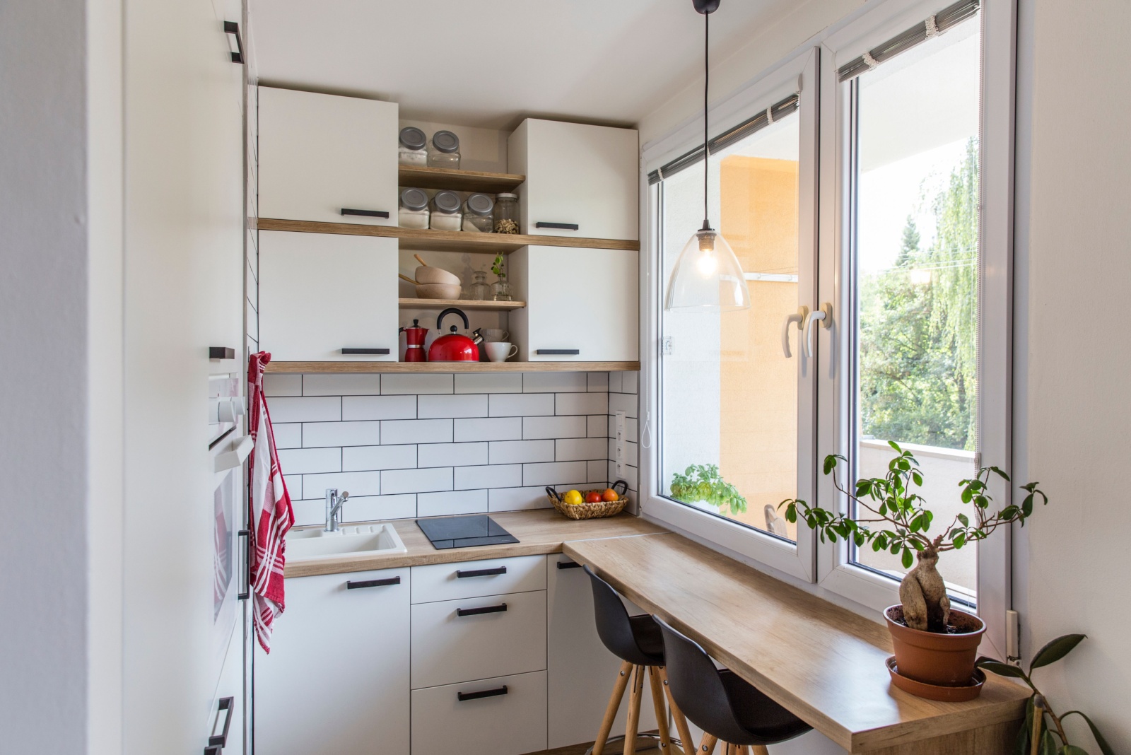 small kitchen with white tiles and white walls, built-in table with two bar stools, white cabinets and a big window