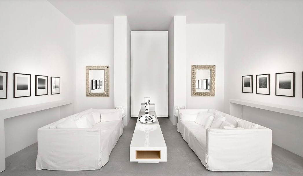 symmetrical living room with two white couches, a white table, two mirrors and black and white artworks