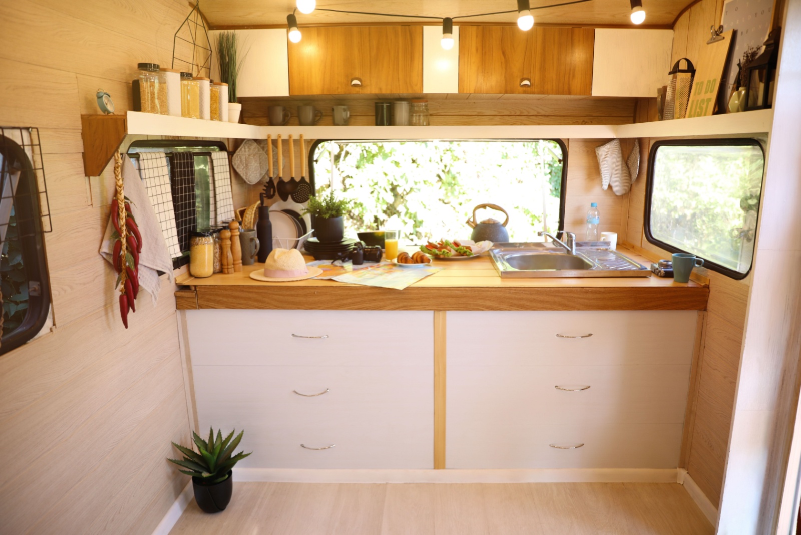 kitchen of a tiny camper with brown countertops, white drawers, a shelf going all round the kitchen