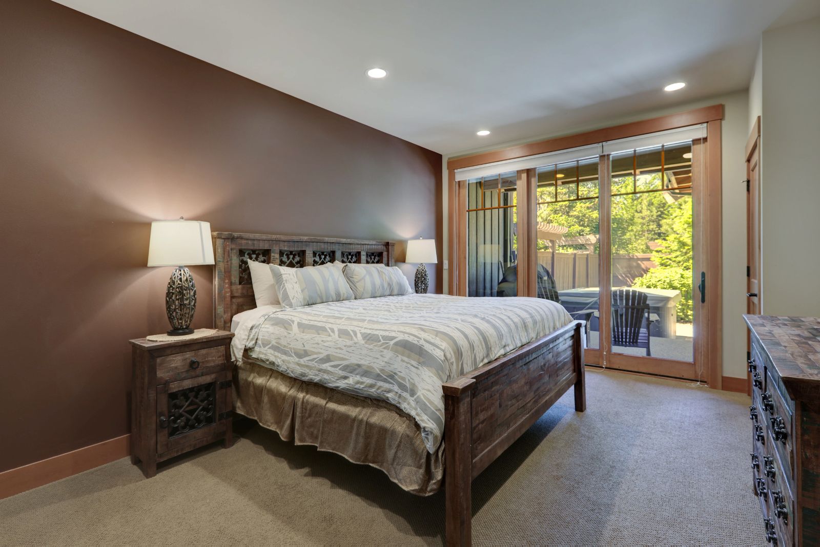 traditional bedroom with a light brown accent wall, other walls in beige, a greyish-wood bed with the same nightstand, doors leading out to the balcony in the back