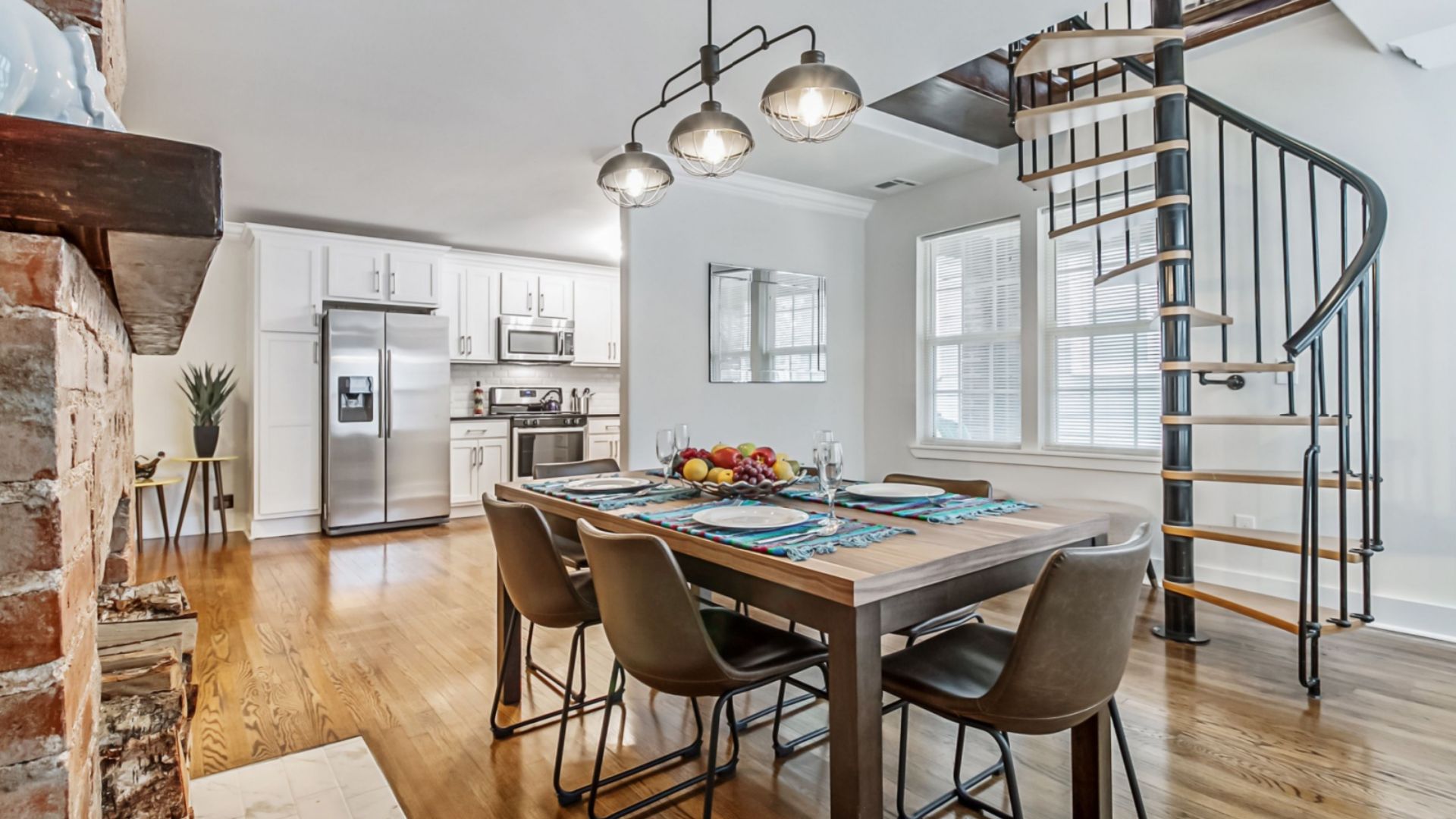 dining room with a dining table and brown chairs and a lamp above and a kitchen in the background