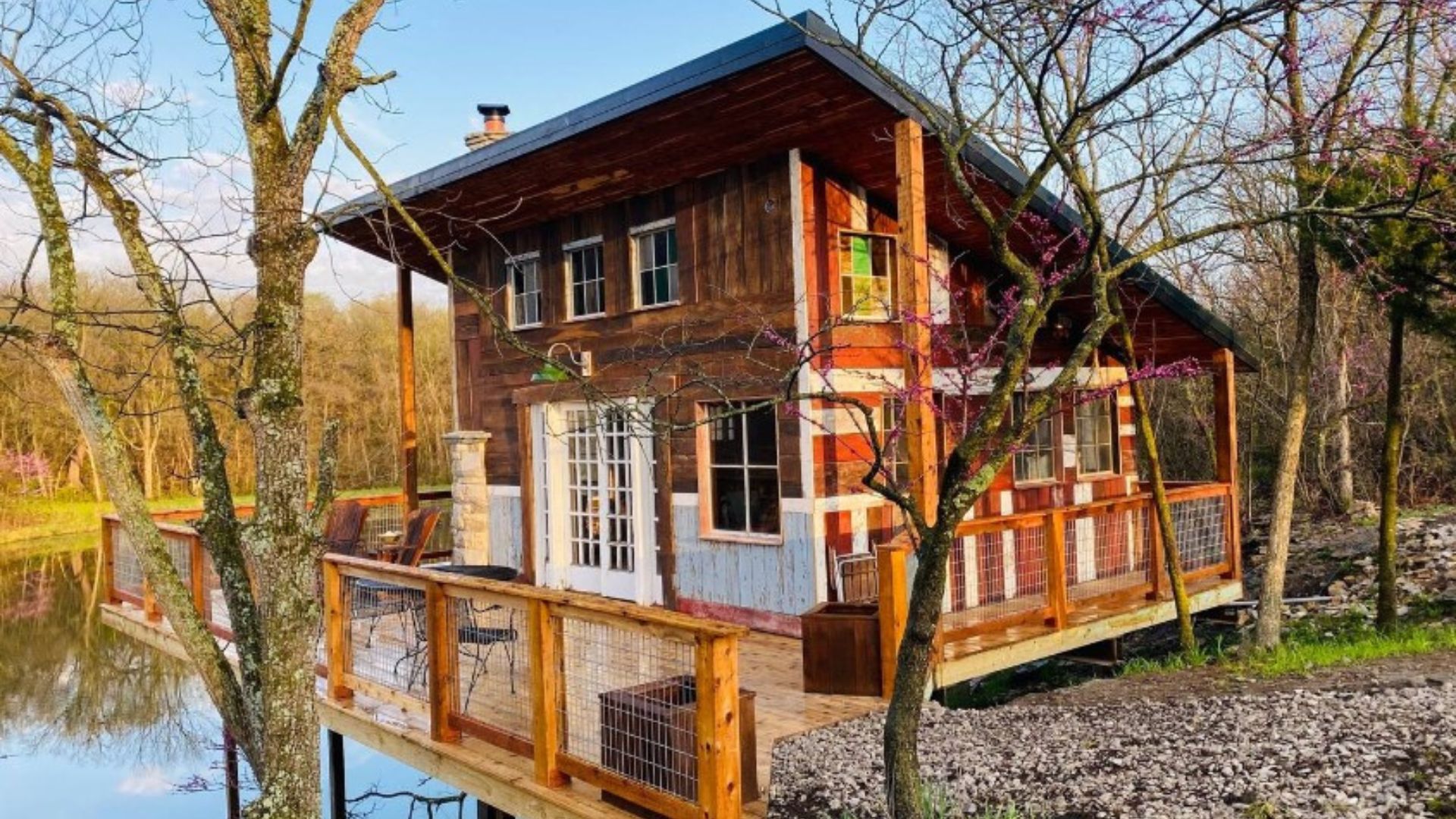 exterior of a cabin with a wraparound deck near the lake