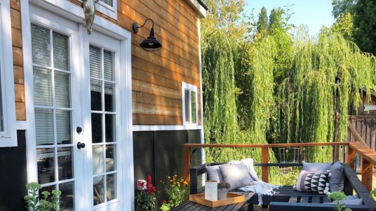 exterior of the THOW with wood siding, windows and french doors in white, a small patio with black furniture by the entrance
