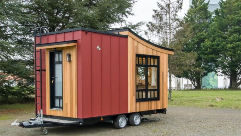a small, modern wooden tiny house on wheels with a red door and a large window