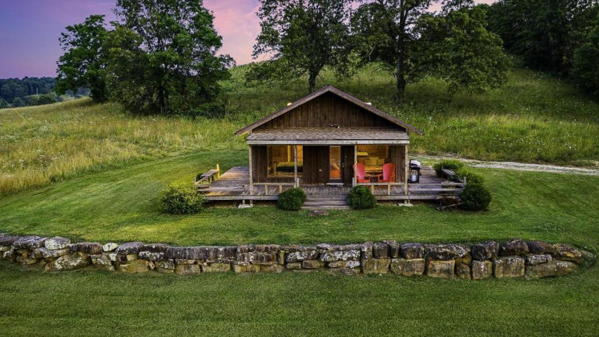 exterior of the small cabin with front porch, surrounded by green fields and trees