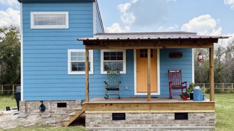 exterior of a tiny house with a blue wall and a mini porch with two rocking chairs