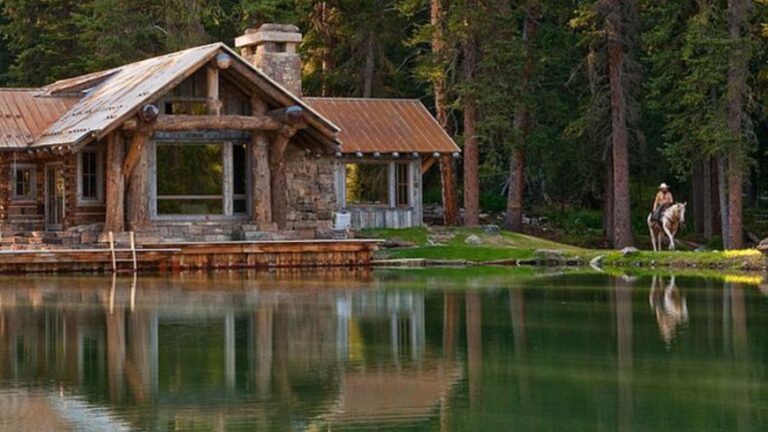 rustic exterior of the log cabin on the private pond, house reflecting in it, pine trees and woods around the house