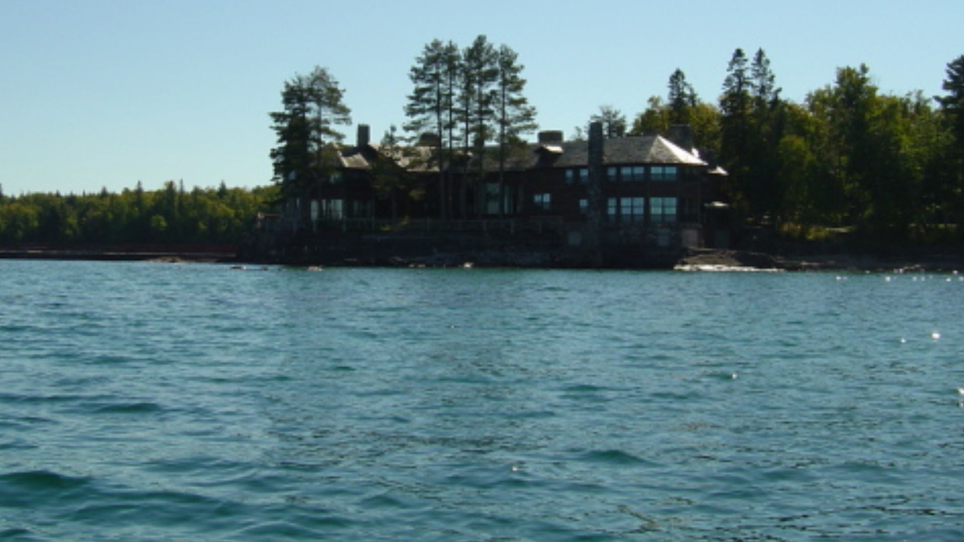 granot loma, a historic stone and log mansion situated on a scenic waterfront surrounded by trees