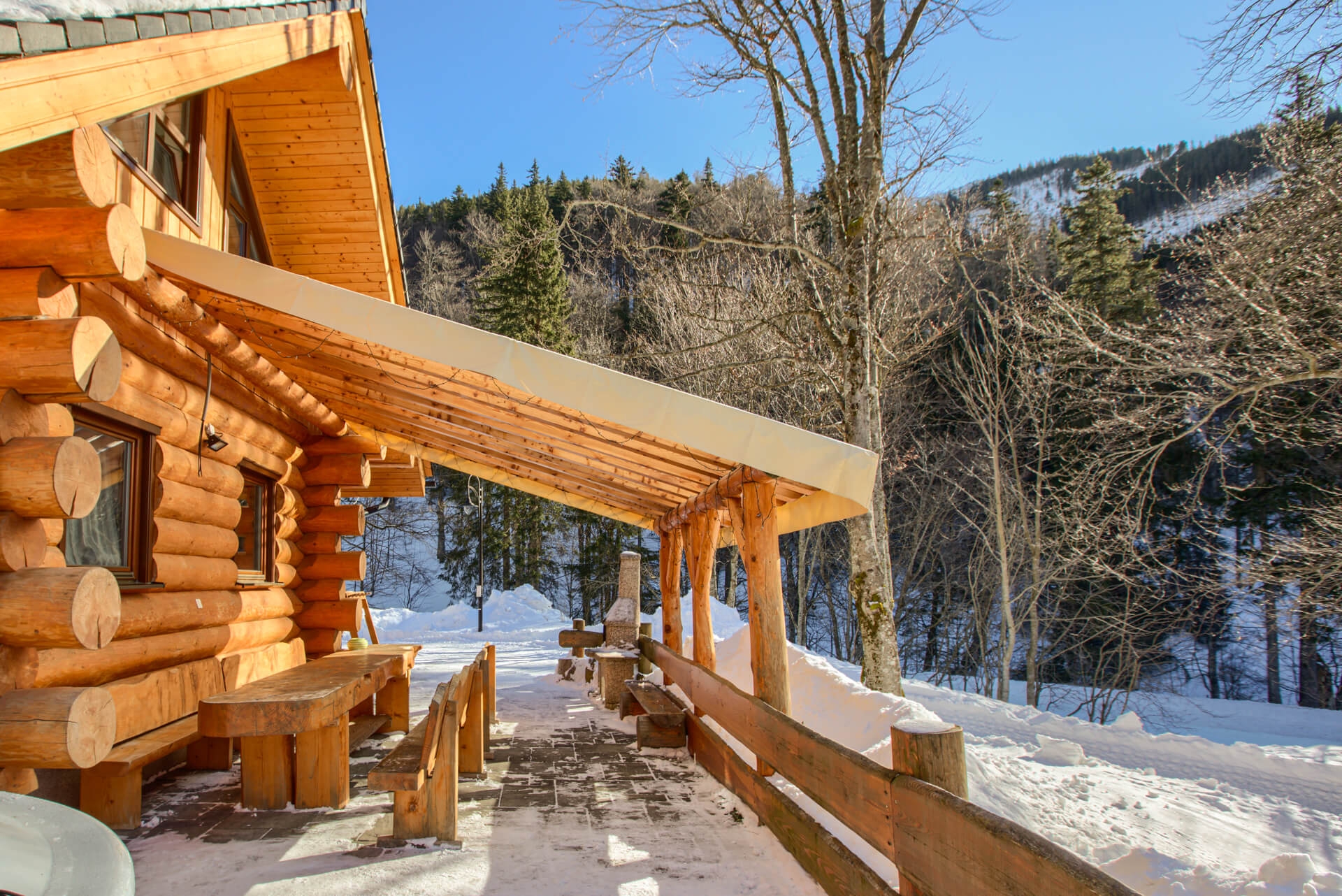 Exterior of a log cabin in winter with wooden table, chairs and a grill