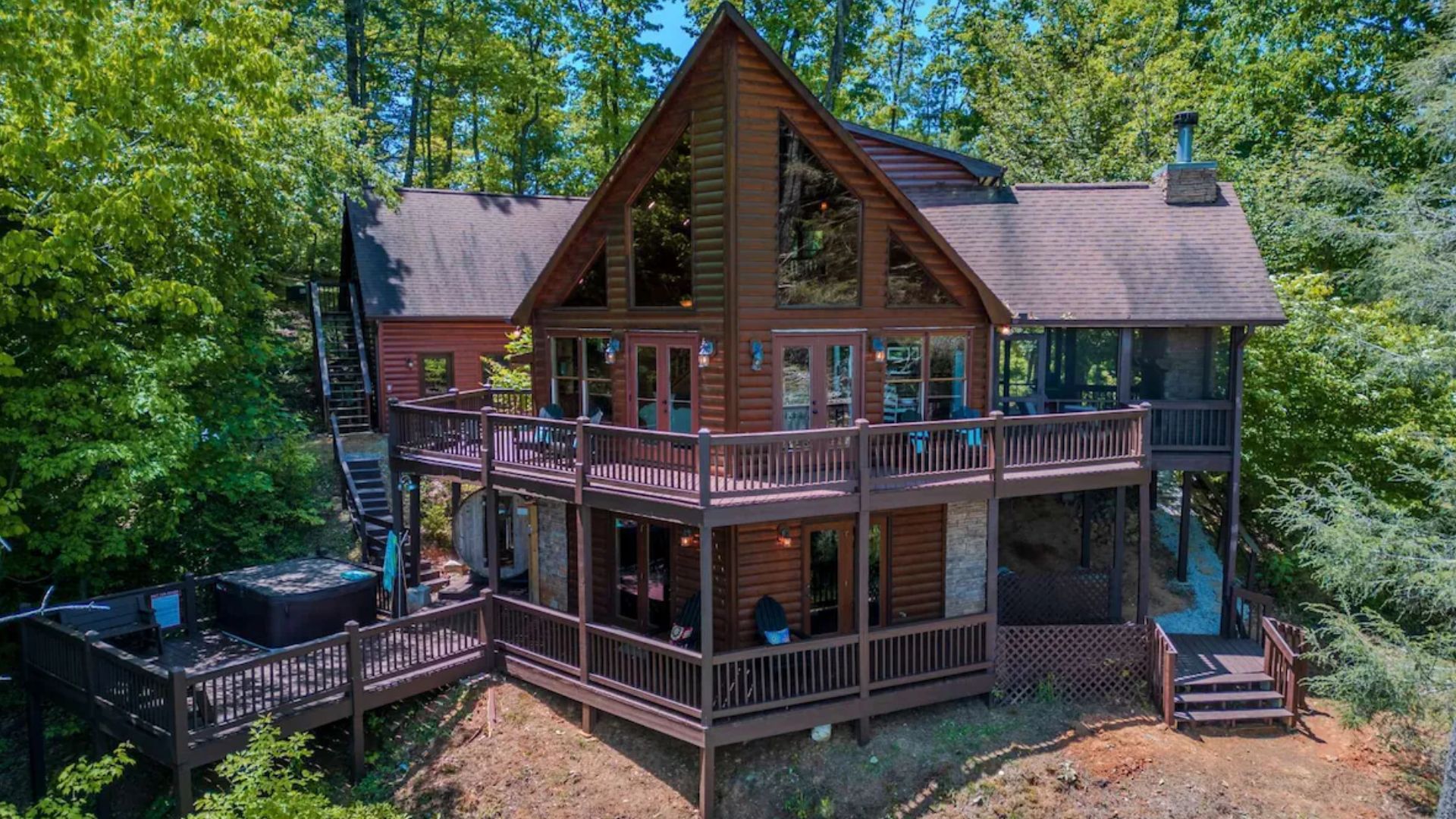 exterior of the cabin in the woods with angled walls, lights on, greenery around the house