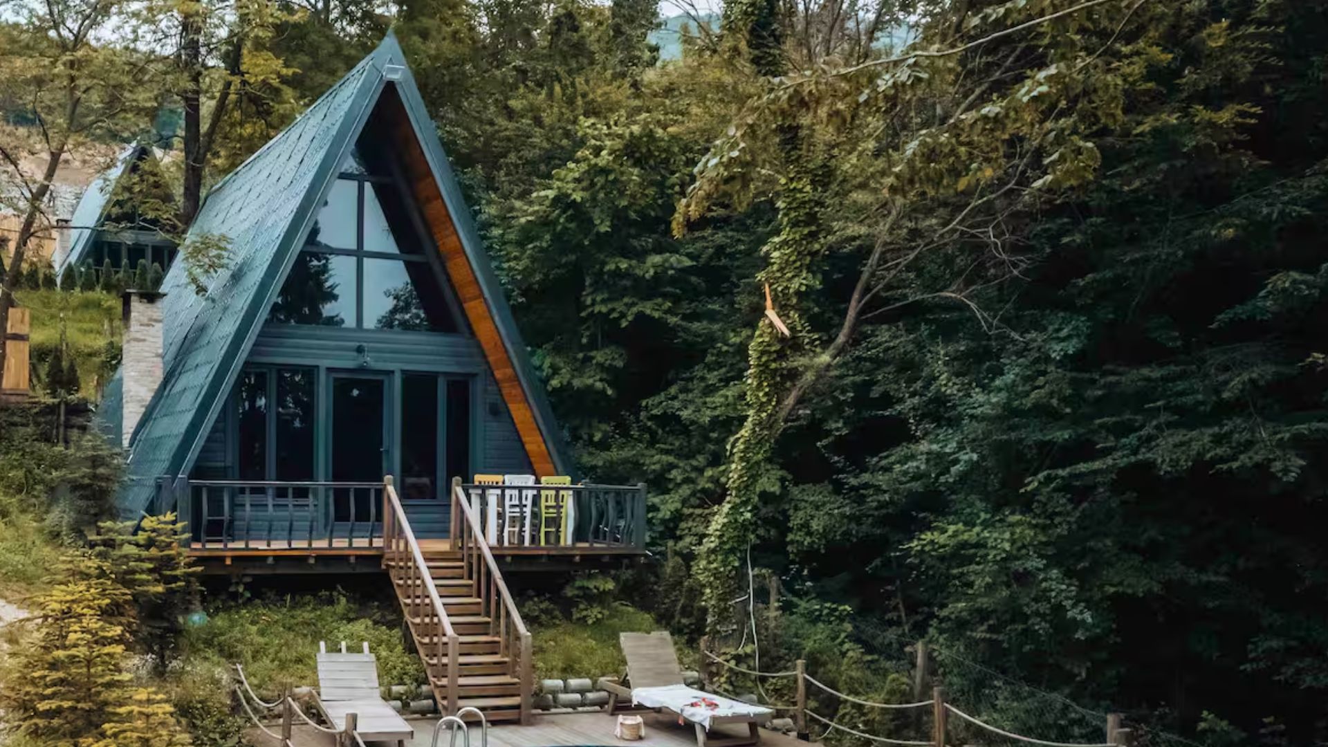 exterior of an a-frame cabin with a pool and deck chairs