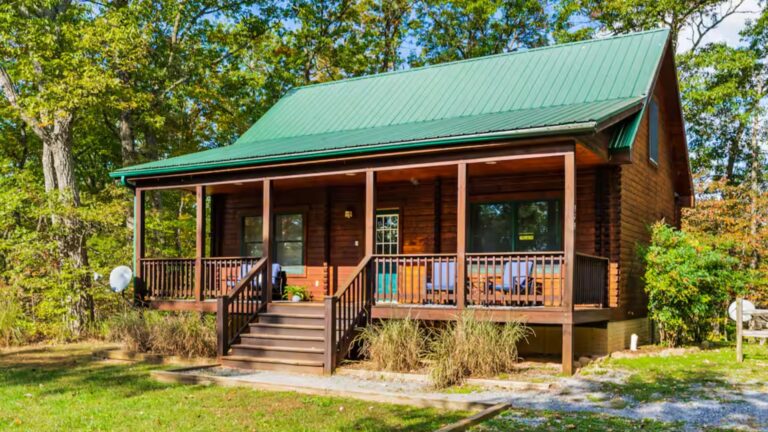 log cabin with a front porch, green roof, and surrounded by trees