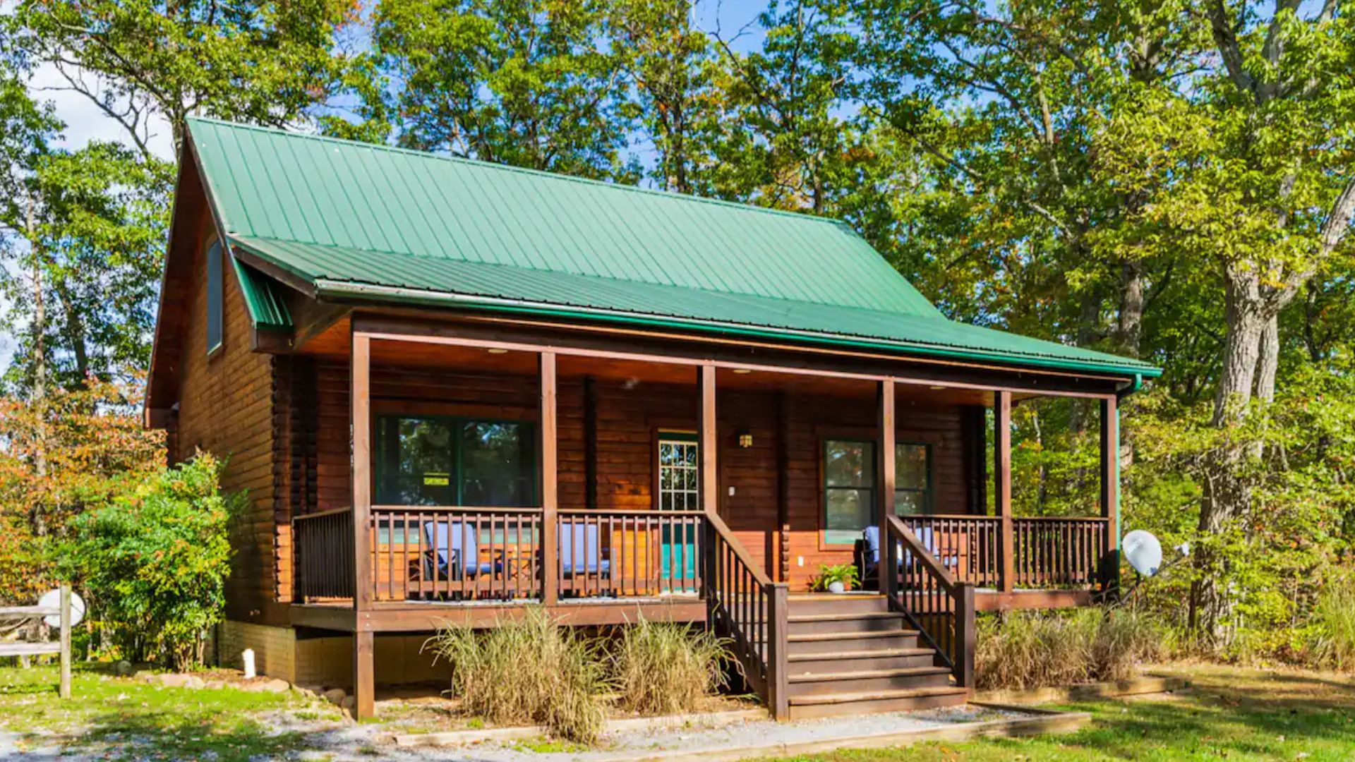 log cabin with a front porch, green roof, and surrounded by trees