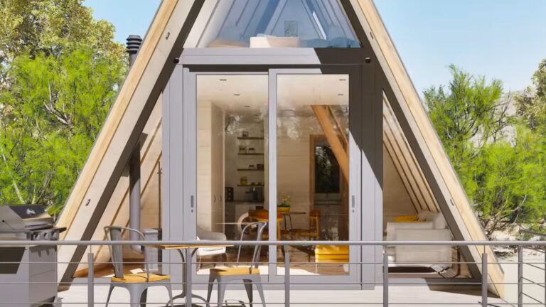exterior of an A-frame shipping container house with a small deck, lots of skylight windows, and the front side completely in glass