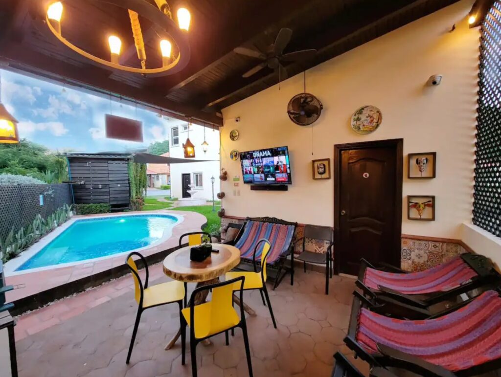 Covered lounge area by the pool with a TV