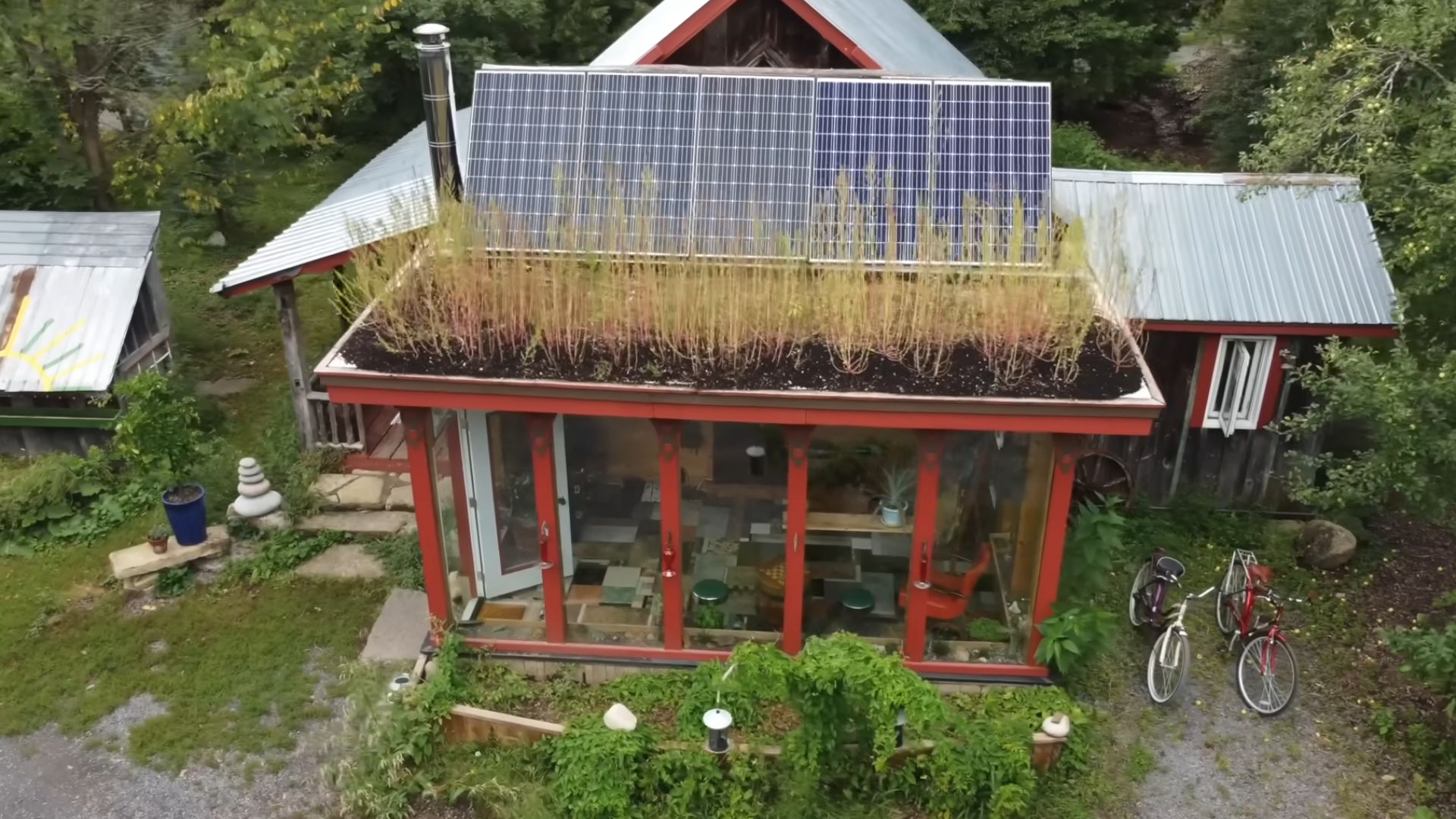 aerial view of the farm cabin in red, with solar panels, surrounded by forest and greenery