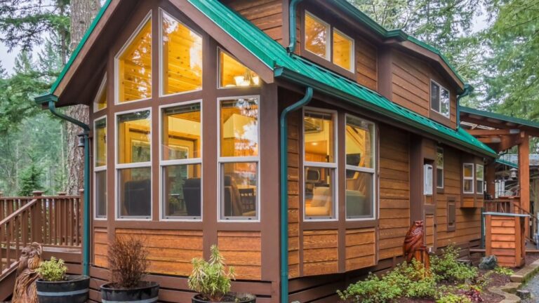 exterior of the cabin in the woods with a small porch, a wall of windows up front and a green roof