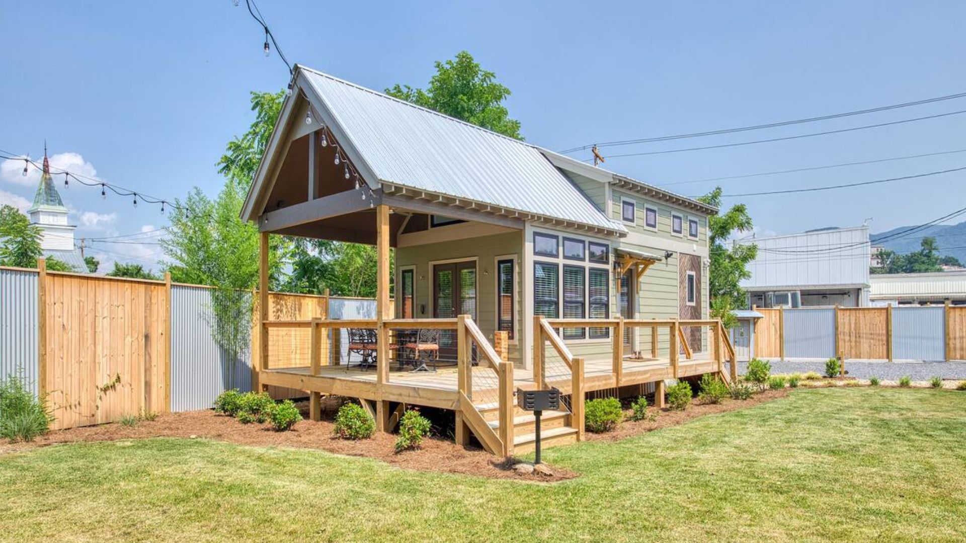 tiny house exterior done in light green, with a small porch, surrounded by green grass and trees