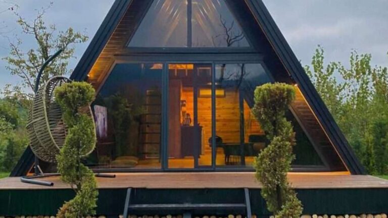 side photo of the A-frame bungalow perla in winter time with a fire pit visible, Christmas tree on the front porch, rocking chairs and some lounge chairs as well