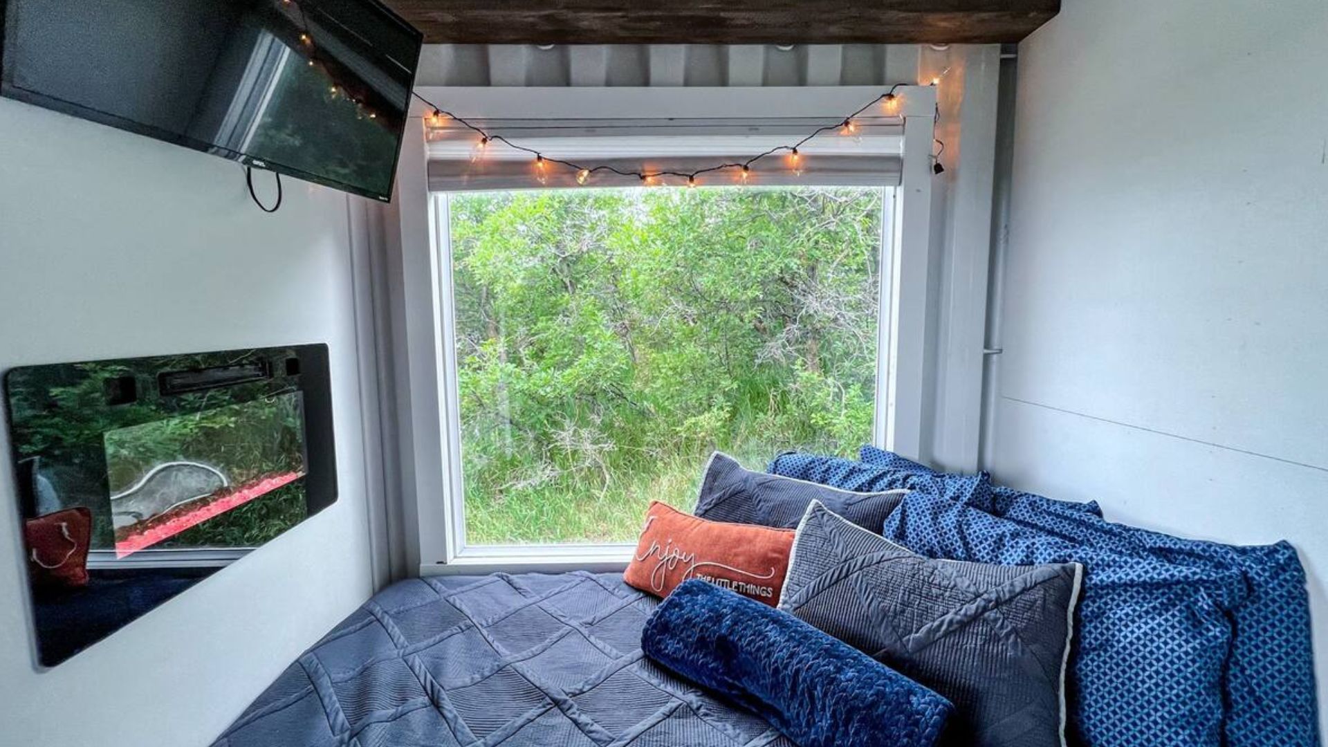 the cizy bed in the corner next to a huge window, fireplace and TV on the wall before it